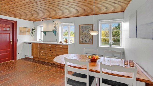 A kitchen with wooden cabinets, a red door, and a dining area with a table and chairs.