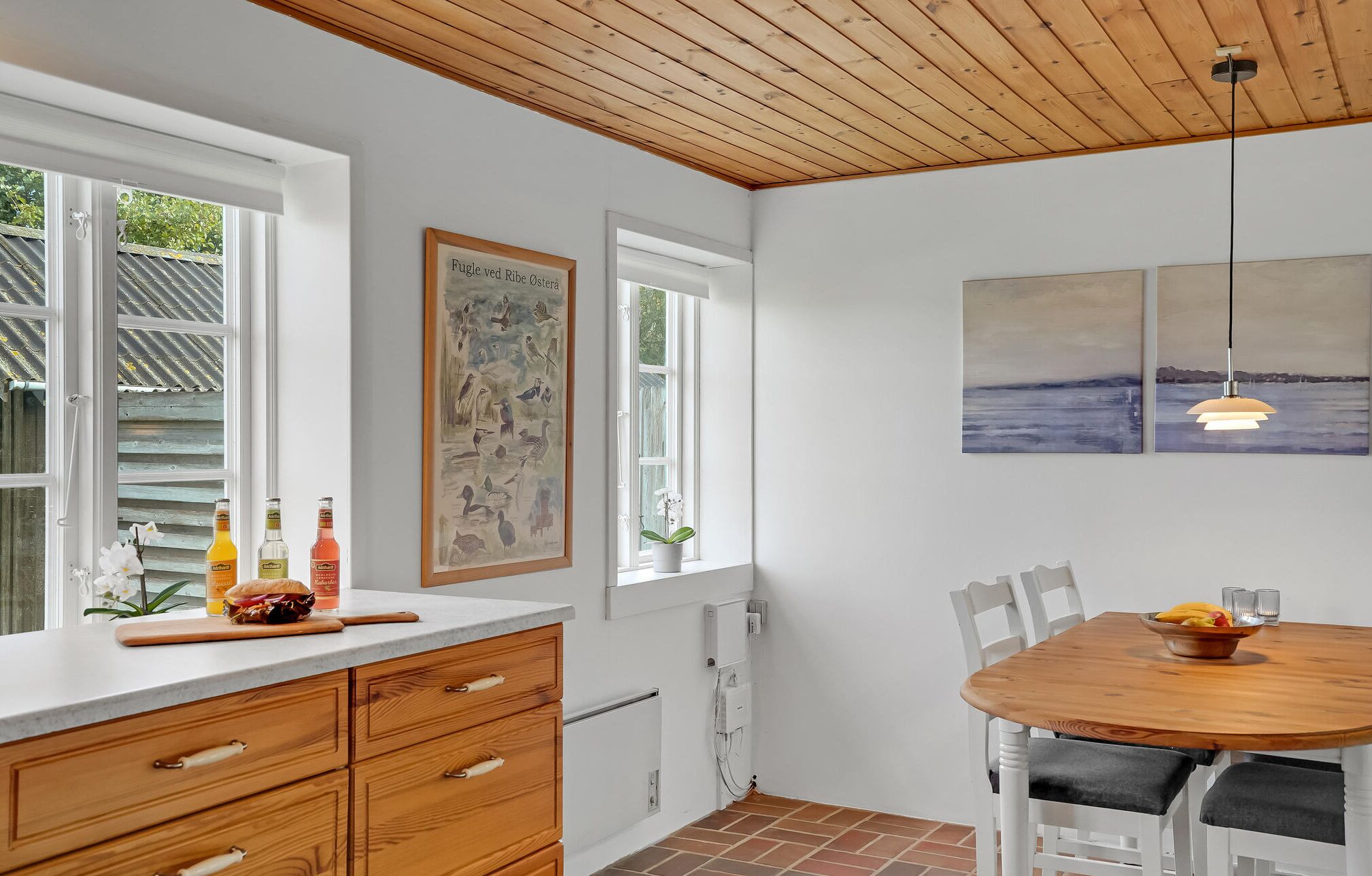 A kitchen with wooden cabinets, a dining table, and artwork on the walls.