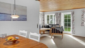 A modern dining area with a wooden table, white chairs, and a fruit bowl.