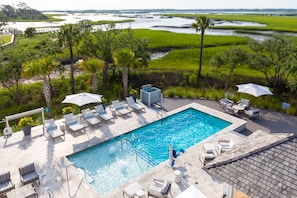 A swimming pool with lounge chairs and umbrellas, surrounded by lush greenery and a view of a water body. - “The Bluebird” (3049 Southerly Way) 2 person creekside bungalow at Kiawah River * EV Charger ~ (Johns Island)