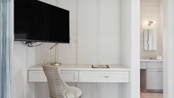 Un escritorio blanco con un televisor montado encima, una silla y un cajón.