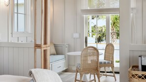 Una habitación con un sofá azul claro, sillas de mimbre, una escalera de madera y un ventanal con vistas a palmeras.