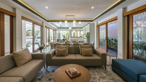 A modern living room with a sofa, a coffee table, and a dining area in the background. - Villa Reillo (Canggu)