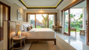 A modern bedroom with a large bed, bedside tables, a lamp, and a view of the outdoors. - Villa Reillo (Canggu)