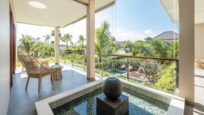 A modern hotel room with a balcony, a small pool, and a view of palm trees and a building in the distance. - Villa Reillo (Canggu)