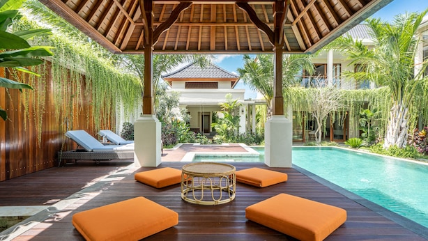 A wooden deck with lounge chairs and a central table, overlooking a swimming pool and lush greenery. - Villa Reillo (Canggu)