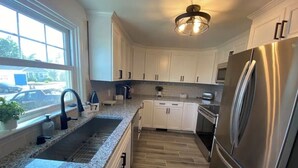 A modern kitchen with white cabinets, a stainless steel refrigerator, granite countertops, and a window providing a view of the outside.