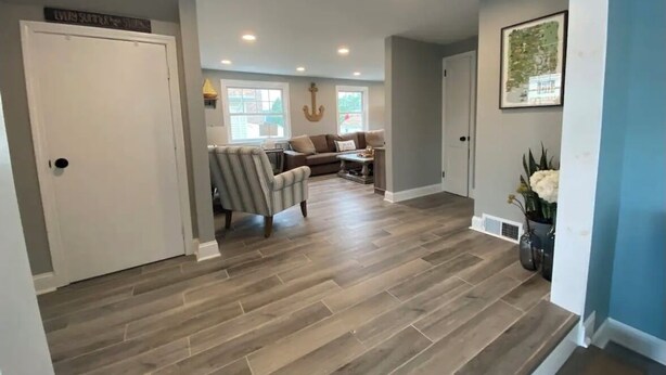 A spacious living area with a herringbone wood floor, a sofa, a chair, and a dining table.