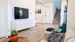 Een moderne woonkamer met een flatscreen televisie, een witte console en een trap naar een ander niveau.