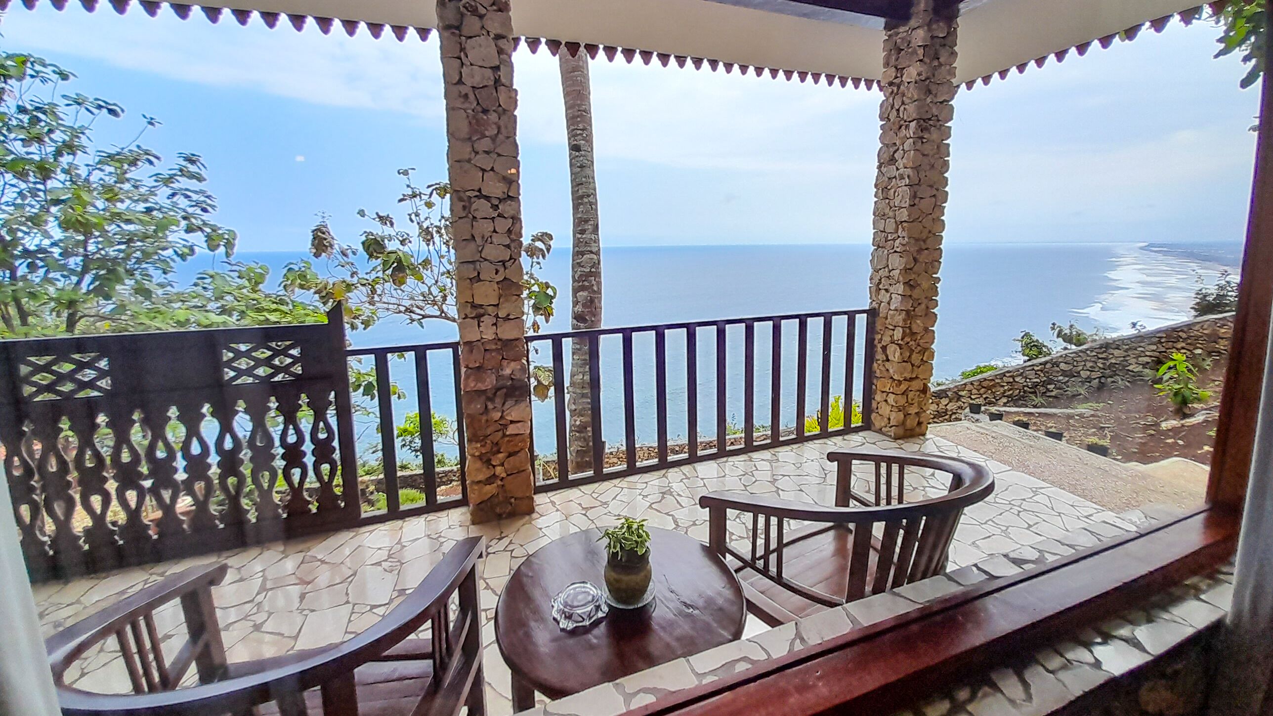 Una terraza con suelo de piedra, una mesa redonda con una planta en maceta y vista al mar.