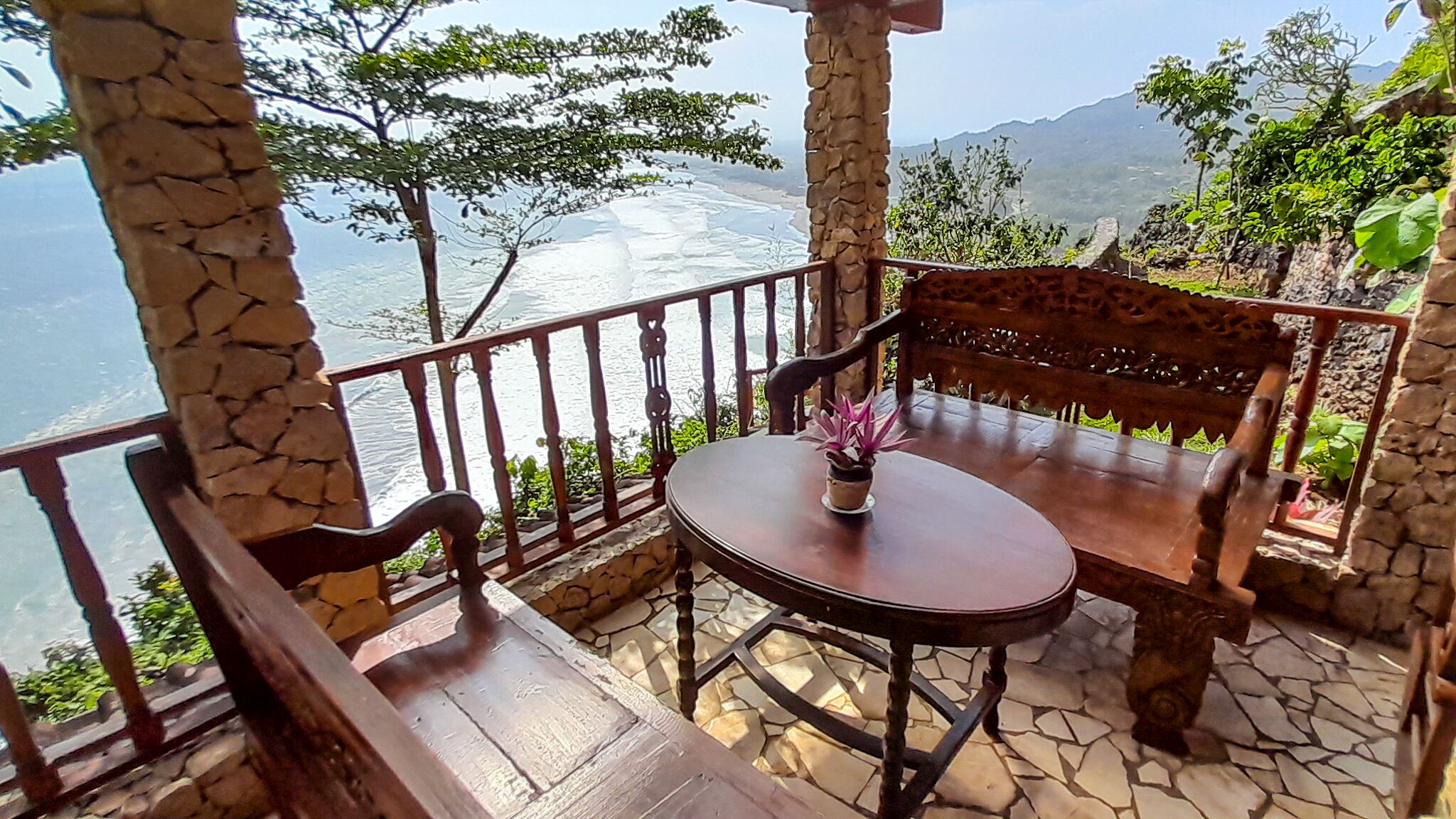 Banco y mesa de madera con una planta en maceta en un balcón con vistas panorámicas.