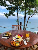 Uma mesa de madeira com uma refeição e uma bebida, com vista para o mar.