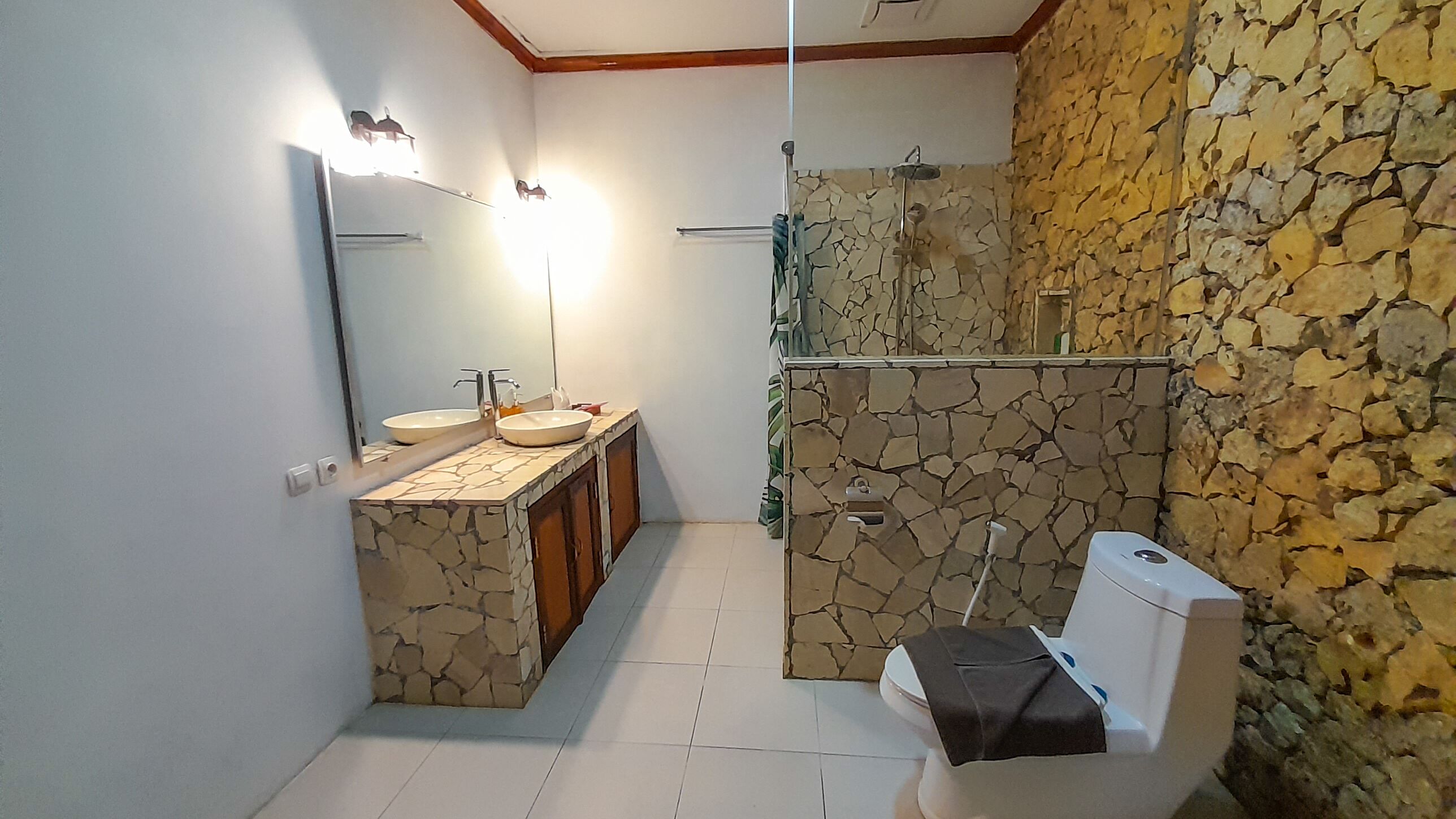 Un bagno con parete in pietra, due lavandini, un water e una doccia.