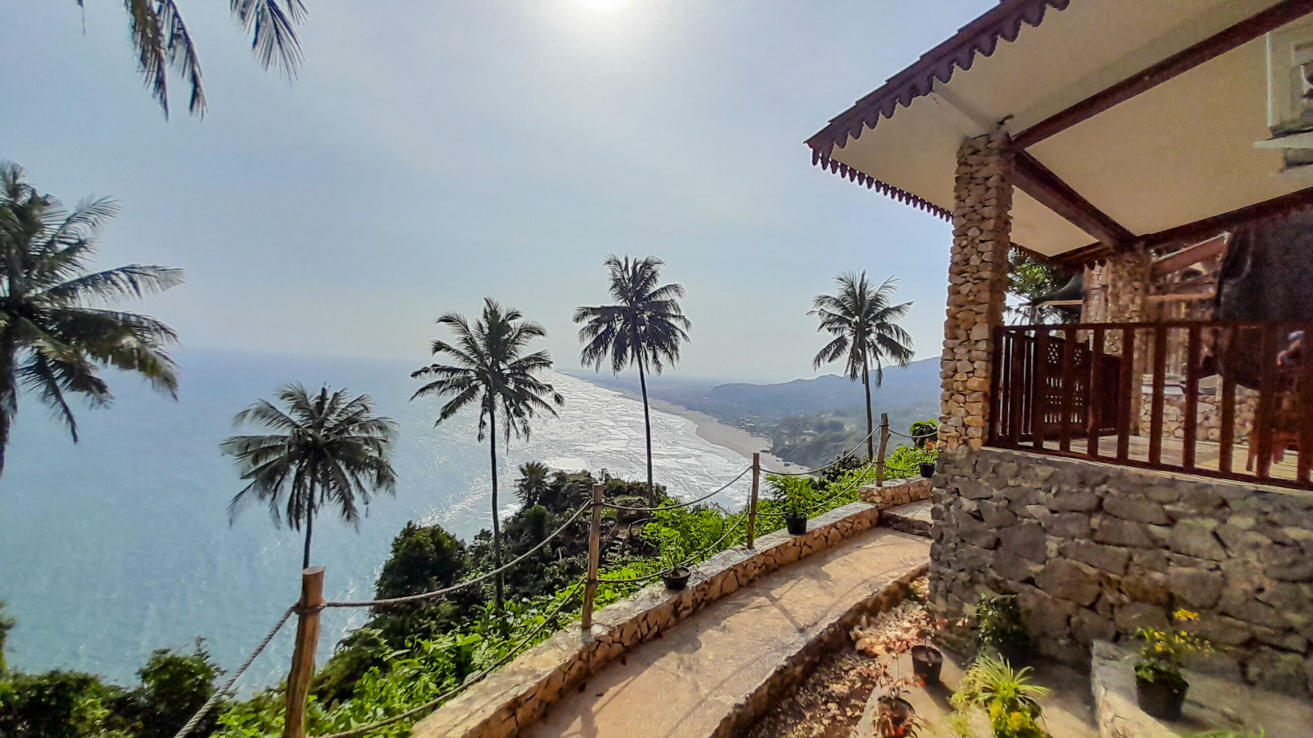 Un bâtiment en pierre doté d’un balcon offrant une vue sur la côte et bordé de palmiers.