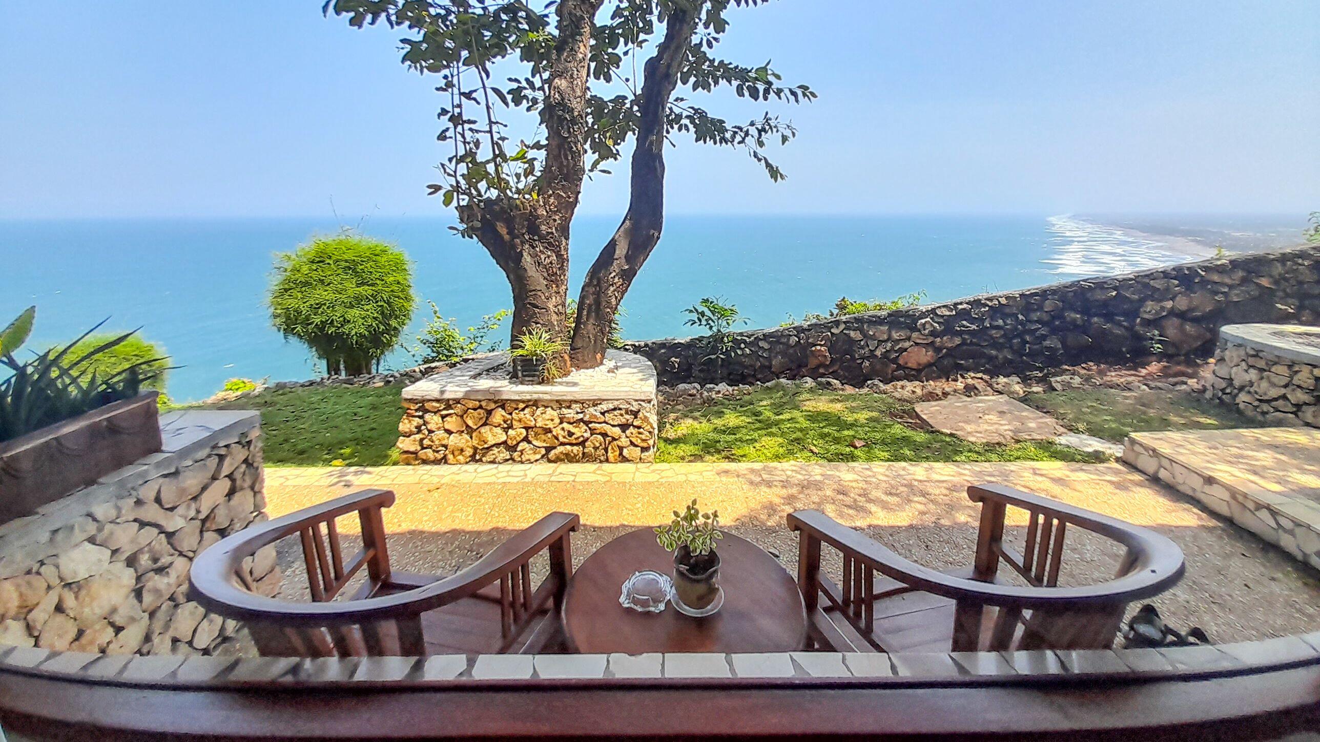Un patio con un muro de piedra, dos sillas de madera y una mesa con una planta en maceta.