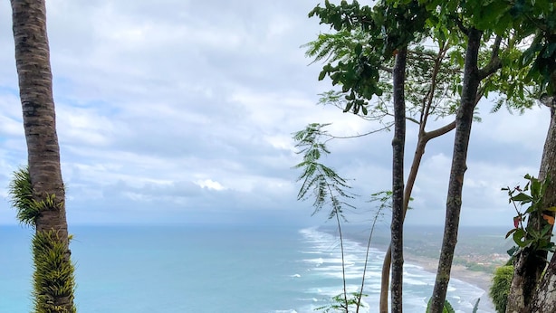 A pool with a breakfast tray containing toast, fruit, and juice, surrounded by trees and overlooking a beach. - Edge Resort Yogyakarta (Giricahyo)