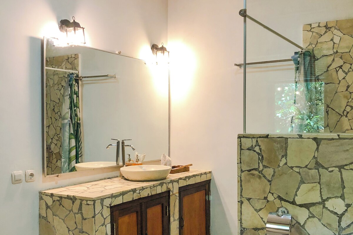A bathroom with a stone sink vanity, a mirror, and a glass-enclosed shower area.