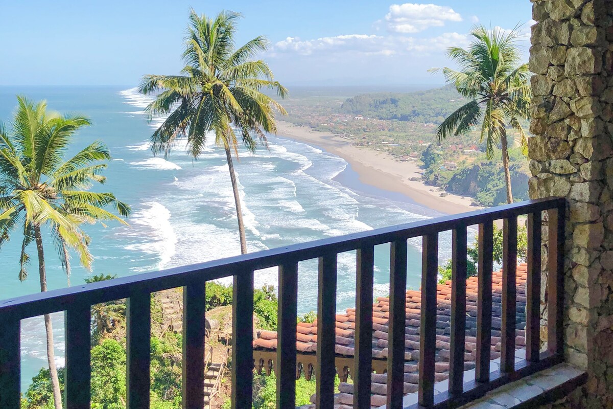A balcony with a stone wall and a view of the ocean.