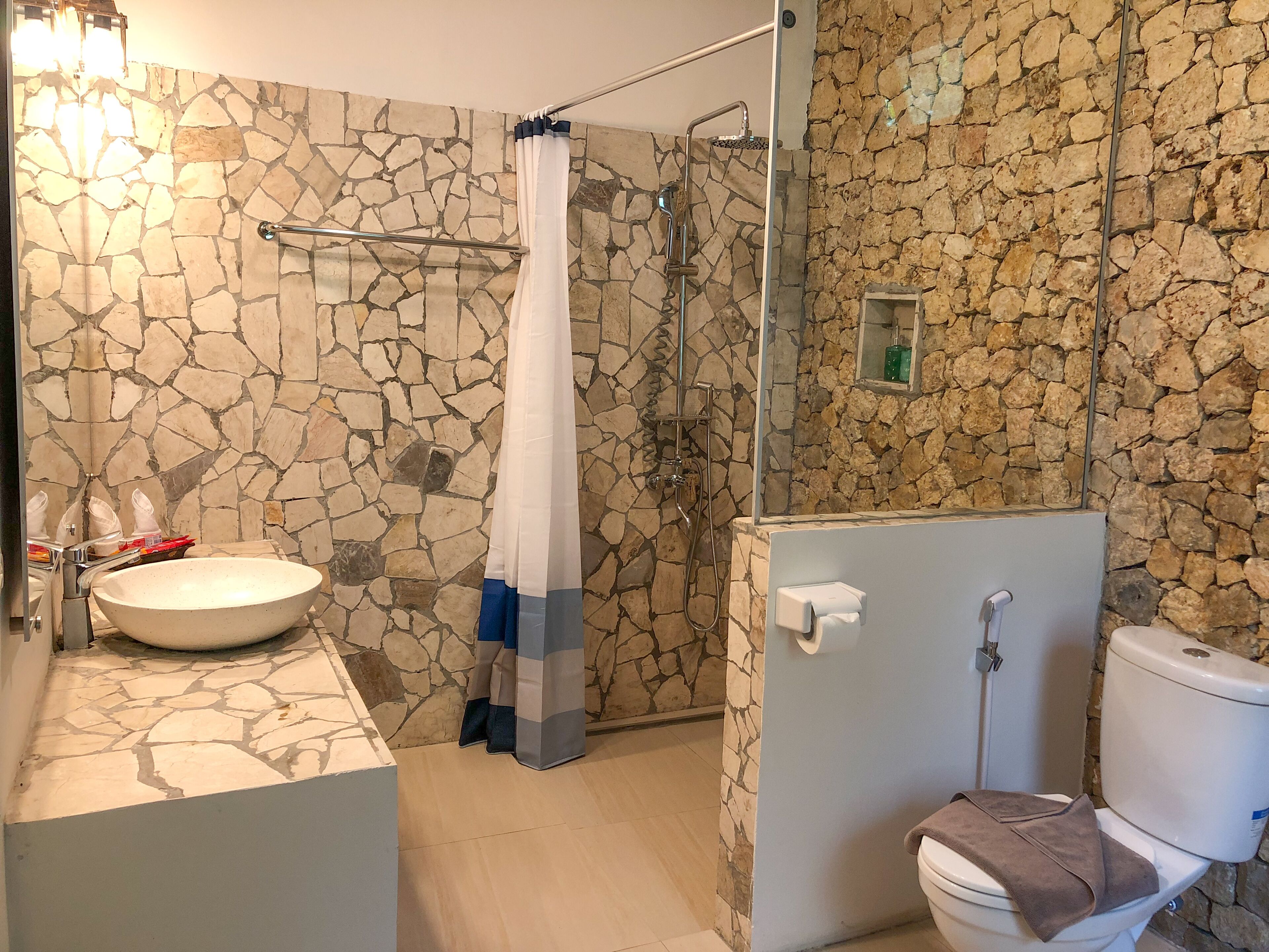 A bathroom with a stone wall, a large sink, a shower with a glass door, and a toilet.