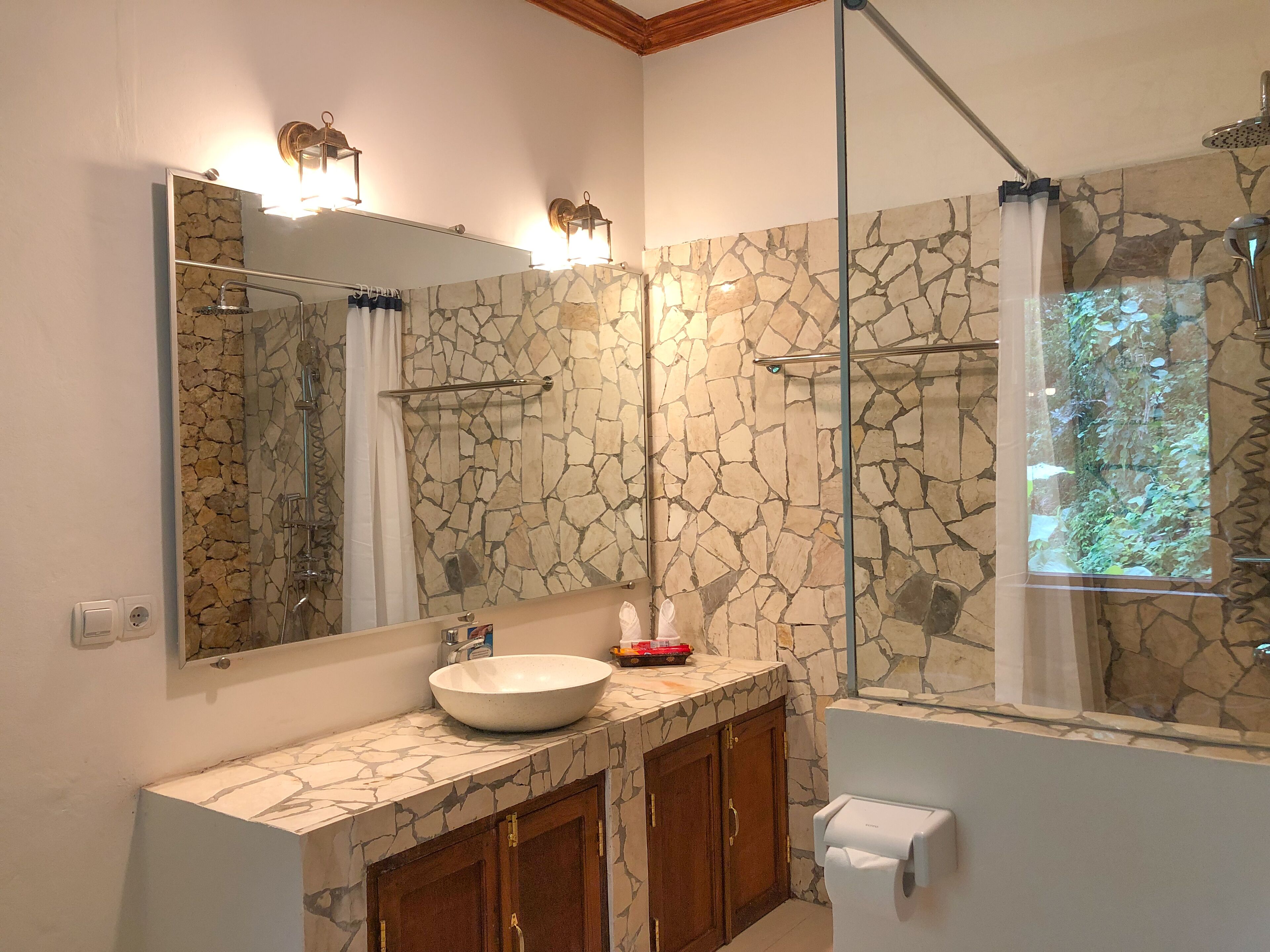 A bathroom with a stone wall, a large mirror, a sink, and a shower with a glass door.