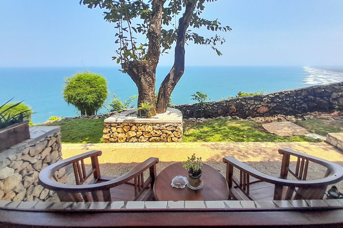A patio with a stone wall, two wooden chairs, and a table with a potted plant.