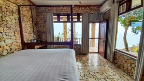 A bedroom with a stone wall, a bed, a desk, and a view of the sea through a balcony door. - Edge Resort Yogyakarta (Giricahyo)