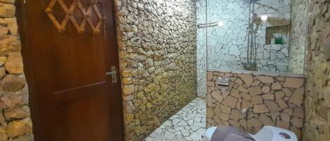 A bathroom with a stone wall, a wooden door, and a tiled floor.