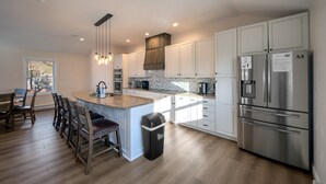 Una cocina moderna con armarios blancos, electrodomésticos de acero inoxidable y una isla central con taburetes de bar.