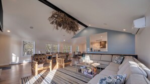 Un amplio salón con un sofá grande, una mesa de centro y una chimenea. Varias ventanas ofrecen luz natural y vistas al exterior.