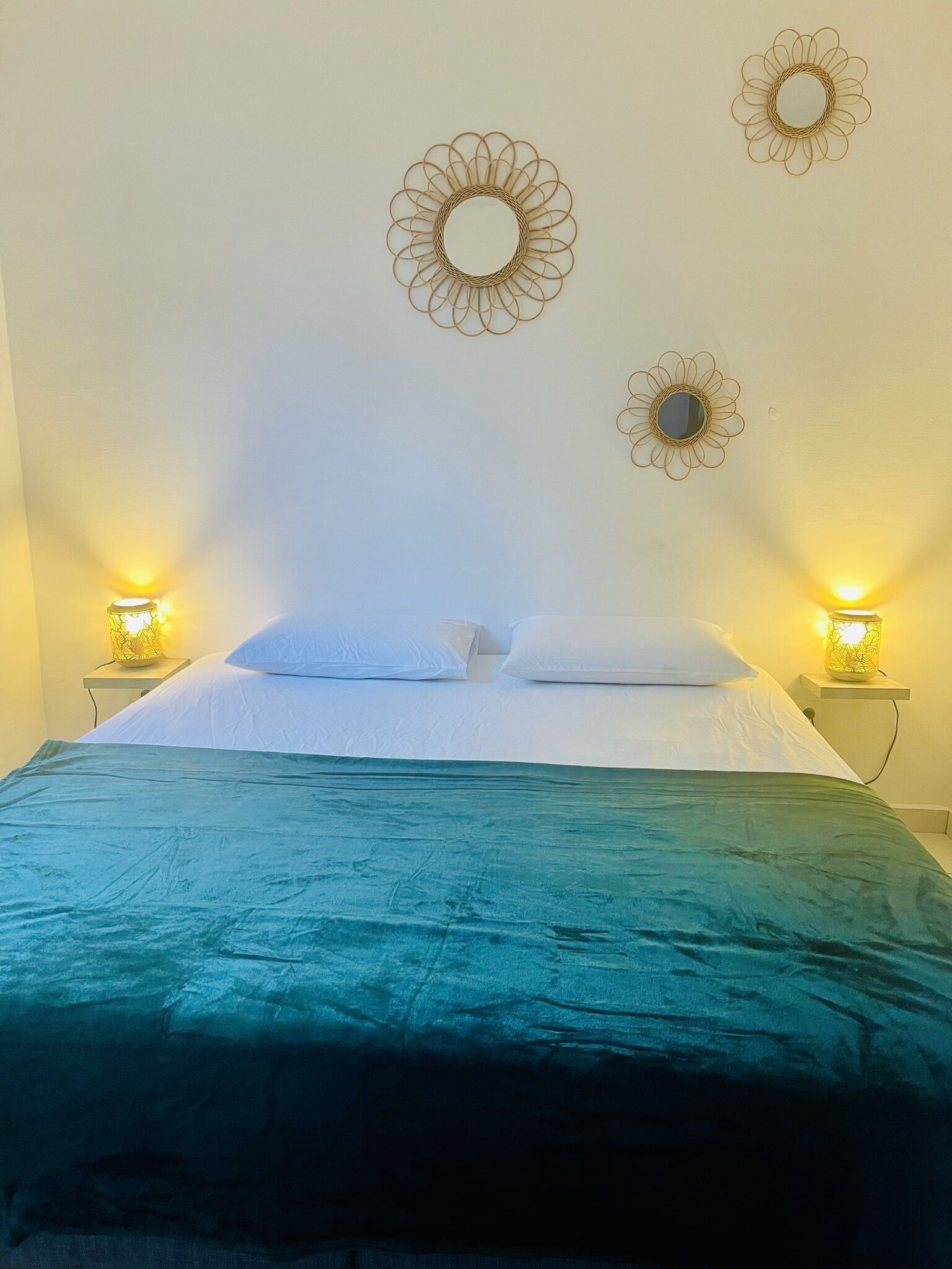 A bed with a teal bedspread, two bedside lamps, and three wall-mounted mirrors.