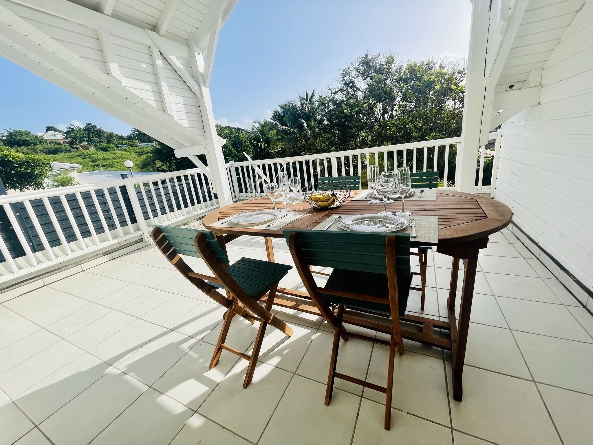 A wooden table set for two with a white railing and greenery in the background.