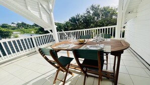 A wooden table set for two with a white railing and greenery in the background. - Lovely, cosy apartment - Right on the water (Le Gosier)