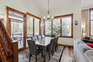 Une salle à manger avec une grande table et des chaises en bois, entourée de grandes fenêtres donnant sur la forêt.