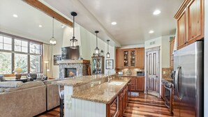 A spacious kitchen with a large island, wooden cabinets, and a stone fireplace.