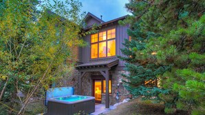 A rustic cabin with a stone foundation, a wooden deck, and a hot tub.