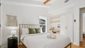 A bedroom with a bed, a bedside table, a lamp, a window, and a door.