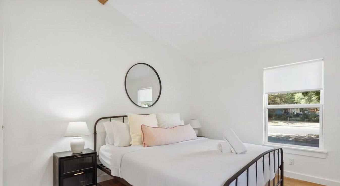 A bedroom with a bed, bedside tables, a mirror, and a window.