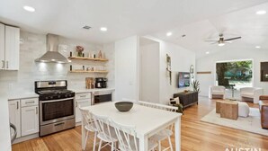 A modern kitchen with white cabinets, a stainless steel stove, and a dining area with a white table and chairs.