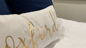 A bed with white and navy blue pillows, one with "Oxford" embroidered in gold. - LOCATION!! LOCATION!! LOCATION!! (Oxford)