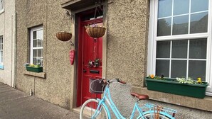 A blue bicycle parked in front of a building with a red door, a window with a white frame, and a green planter box with flowers. - NewburghAprtment/Scotland/sleeps 4/FirePit/Garden (Newburgh)