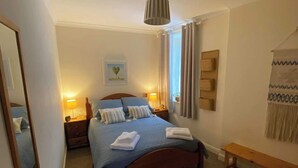 A neatly arranged bedroom with a wooden bed, two bedside tables with lamps, a mirror, a wall-mounted artwork, and a bench. - NewburghAprtment/Scotland/sleeps 4/FirePit/Garden (Newburgh)