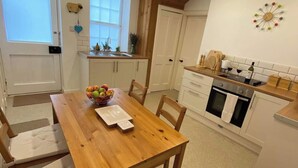 A compact kitchen with white cabinets, a wooden dining table, and a fruit bowl. - NewburghAprtment/Scotland/sleeps 4/FirePit/Garden (Newburgh)