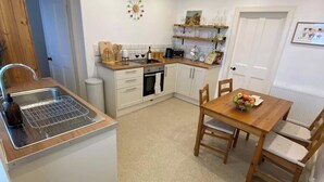 A compact kitchen with a sink, stove, and wooden dining table with chairs. - NewburghAprtment/Scotland/sleeps 4/FirePit/Garden (Newburgh)