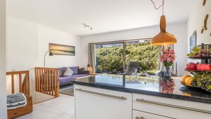 Eine moderne Küche mit großem Fenster, ein Essbereich mit Tisch und Stühlen sowie eine Wohnbereich mit Sofa und Sessel.