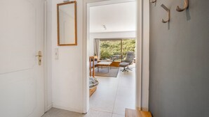 Ein Flur, der in einen Wohnbereich mit Blick ins Freie führt, mit einer Holzbank und einem Spiegel an der Wand.