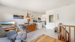 Ein moderner Wohnbereich mit Essplatz, Küche und einem großen Fernseher, der eine Strandansicht zeigt.