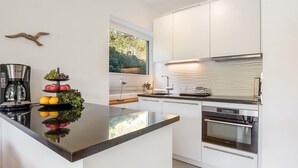 Eine moderne Küche mit einer zentralen Kochinsel, Edelstahlgeräten und Blick ins Freie durch ein großes Fenster.