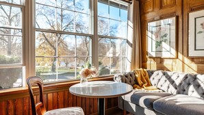 Ein Zimmer mit einem großen Fenster, einem runden Tisch, einer gepolsterten Couch und einem gerahmten Bild an der Wand.