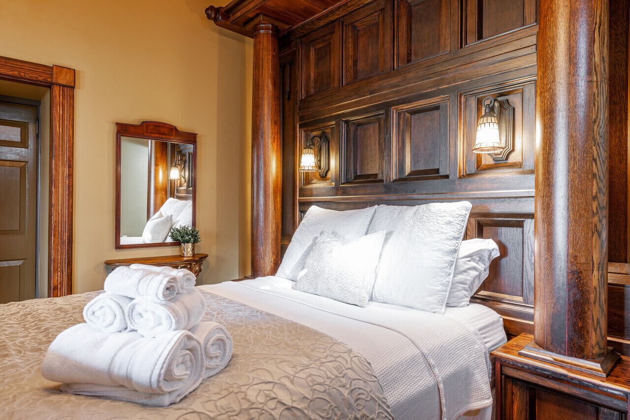 A hotel room with a large bed, wooden headboard, a mirror, and a nightstand with a lamp.