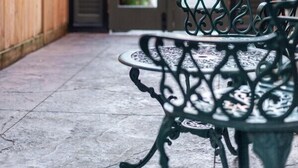 Eine Terrasse mit einem Metalltisch und einer Bank, einem Holzzaun und einer Tür zu einem überdachten Eingang.